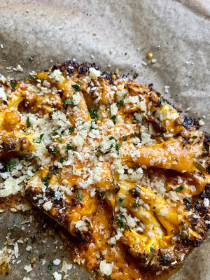 A large cauliflower steak or slice with nicely charred edges, covered in melted orange cheese with a crunchy parmesan crumb and parsley flakes.