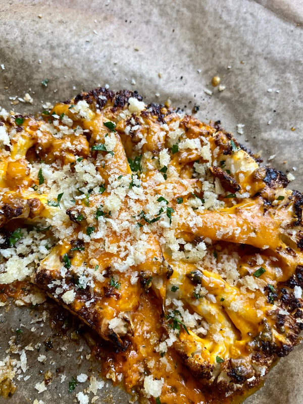 A large cauliflower steak or slice with nicely charred edges, covered in melted orange cheese with a crunchy parmesan crumb and parsley flakes.