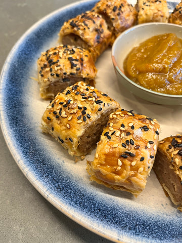 homemade crispy sausage rolls and on a placte with bagel seasoning on top and a bowl of chutney