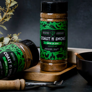 Spice jars with green labels sitting on a chopping boards with kitchen items