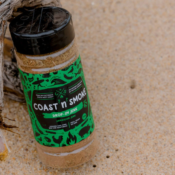 Spice jar with a bright green label sitting on the beach against drift wood