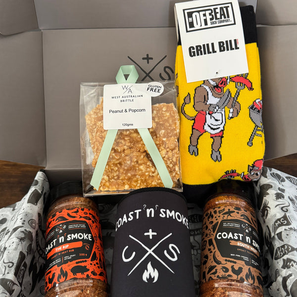 Box containing various items including 2 bbq rubs,  a yellow bbq themed socks, a black stubby holder with white design, and a bag of popcorn and peanut brittle.