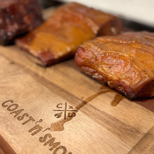 Wooden cutting board with 'Coast n Smoke' branding and smoked fish on a blurred background