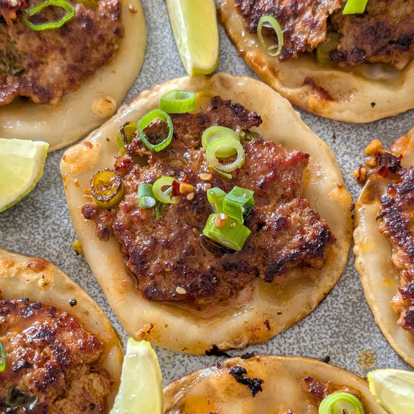 Smash dumplings with meat filling and green onions, garnished with lime wedges.