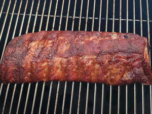 Rack of ribs rubbed in The Rip on a BBQ grill - rich mahogany colour ribs