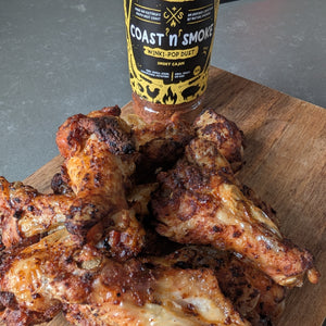 crispy chicken wings on a wooden board with a bottle of Coast 'N Smoke hot sauce.
